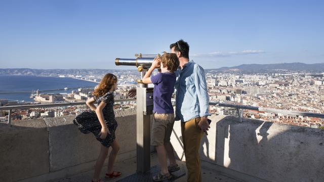 Visite en famille de notre Dame de la garde, enfant qui regarde dans la longue vue, Marseille en arrière plan