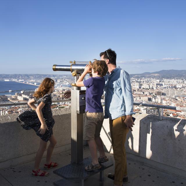 Visite en famille de notre Dame de la garde, enfant qui regarde dans la longue vue, Marseille en arrière plan