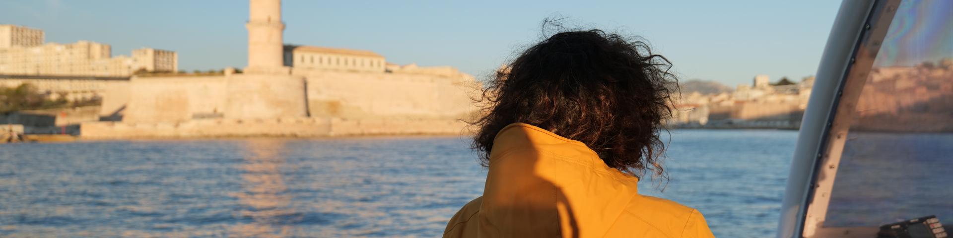 Personne en ciré jaune sur un bateau arrivant dans le port de Marseille, devant le fort St Jean