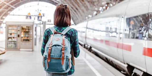Une jeune touriste avec un sac à dos attend son train dans une gare