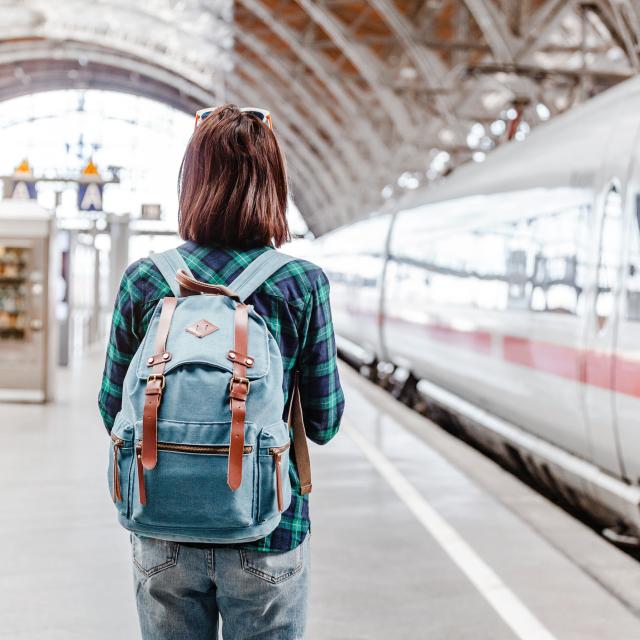 Une jeune touriste avec un sac à dos attend son train dans une gare