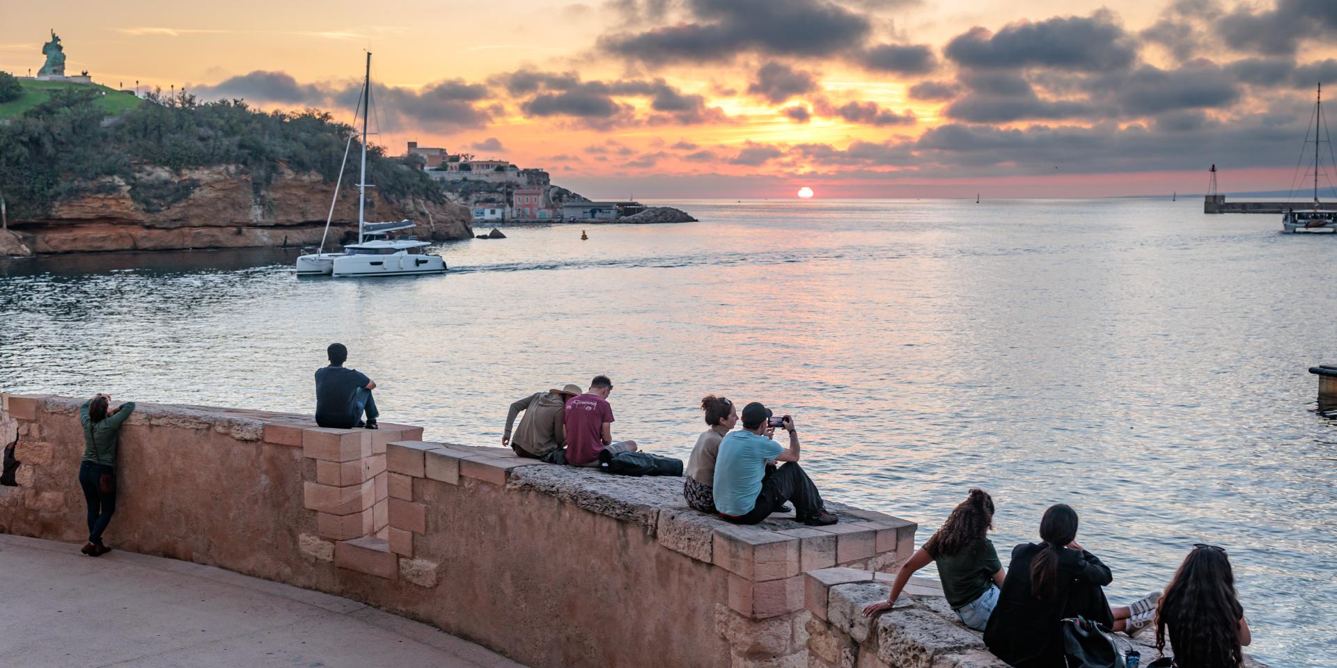 personne assise sur muret qui regardent le coucher de soleil depuis le Fort St jean