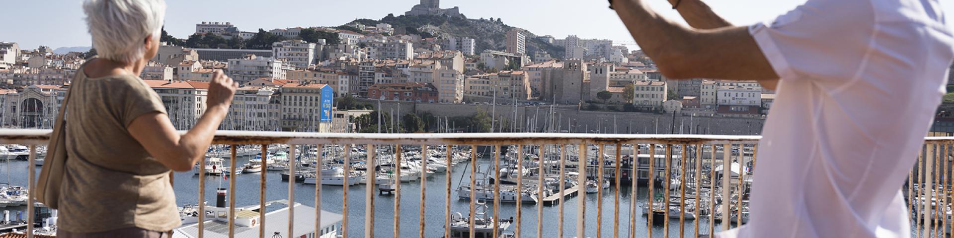 Senior en visite à Marseille prenant une photo du Vieux-Port