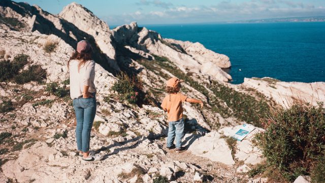 Adulte et enfant marchant sur un paysage rocheux face à la mer sur l'ile du Frioul a amarseille