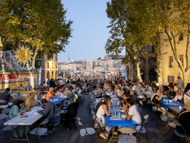 Personnes en train de diner a l'exterieur sur de grande table pour le Kouss Kouss Festival a marseille